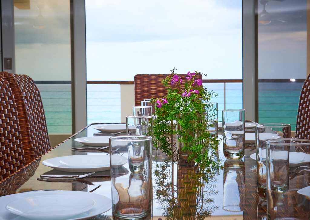 Mesa de comedor puesta frente a ventanales al mar